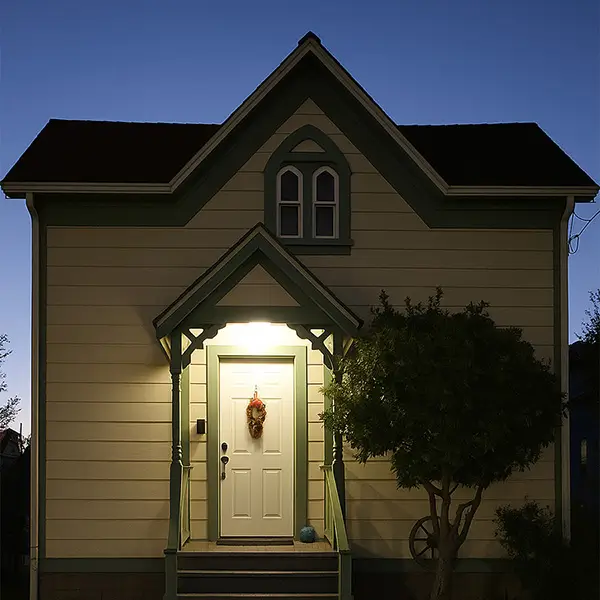 A small cream-colored house with green trim glows under a porch light at dusk in Eureka, California. A wreath decorates the front door, and a tree stands beside the entrance against a dark blue sky.